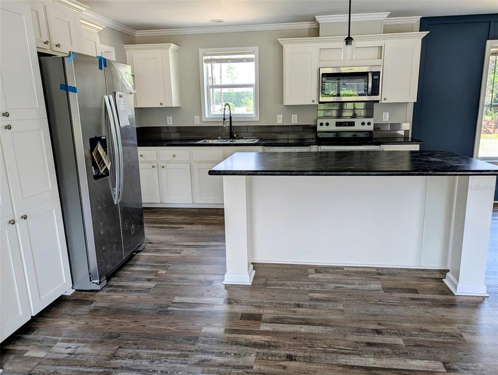 A kitchen features white cabinets, a dark island countertop, stainless steel appliances, and wood-look flooring — 26125 COUNTY ROAD 44A, EUSTIS, FL
