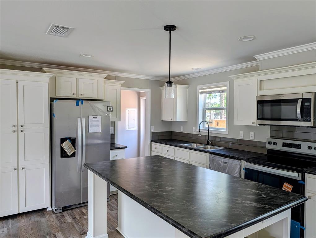 A kitchen features white cabinets, a large dark countertop island, and stainless steel appliances — 26125 COUNTY ROAD 44A, EUSTIS, FL