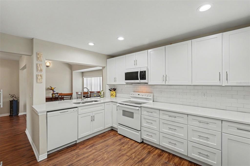 A kitchen with white cabinets, white countertops, a subway tile backsplash, and wood-look flooring — 13507 PALMWOOD LANE UNIT 13507, TAMPA, FL
