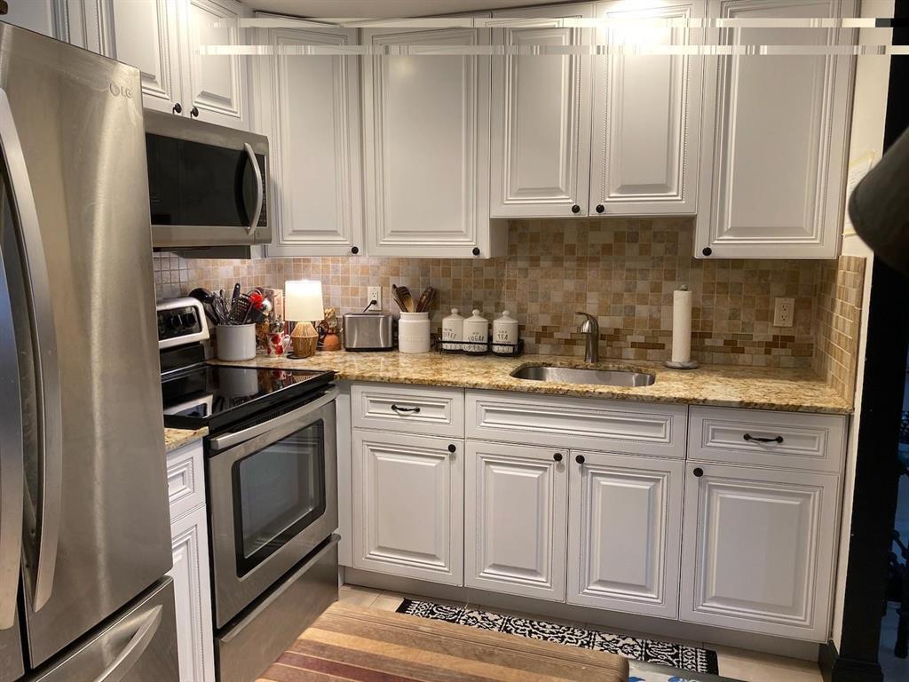 A kitchen features white cabinetry, granite countertops, stainless steel appliances, and a tiled backsplash — 491 Brittany K, Delray Beach FL 33446, DELRAY BEACH, FL