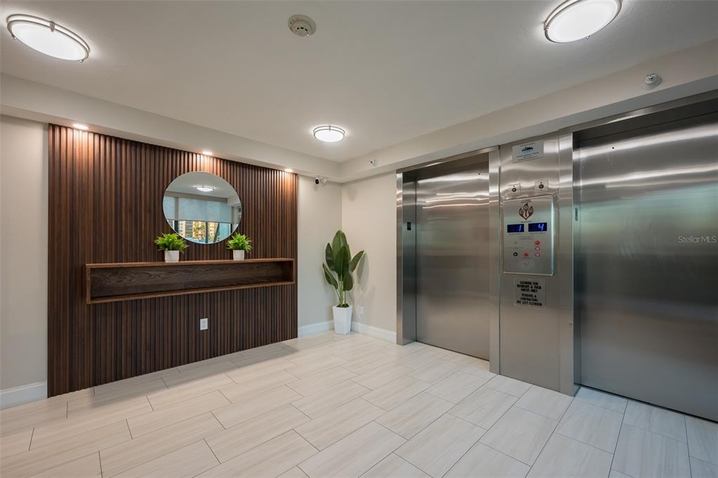 An elevator lobby features wood-slat wall paneling, a floating shelf, and light-colored tile flooring — 5780 MIDNIGHT PASS ROAD UNIT 210, SARASOTA, FL