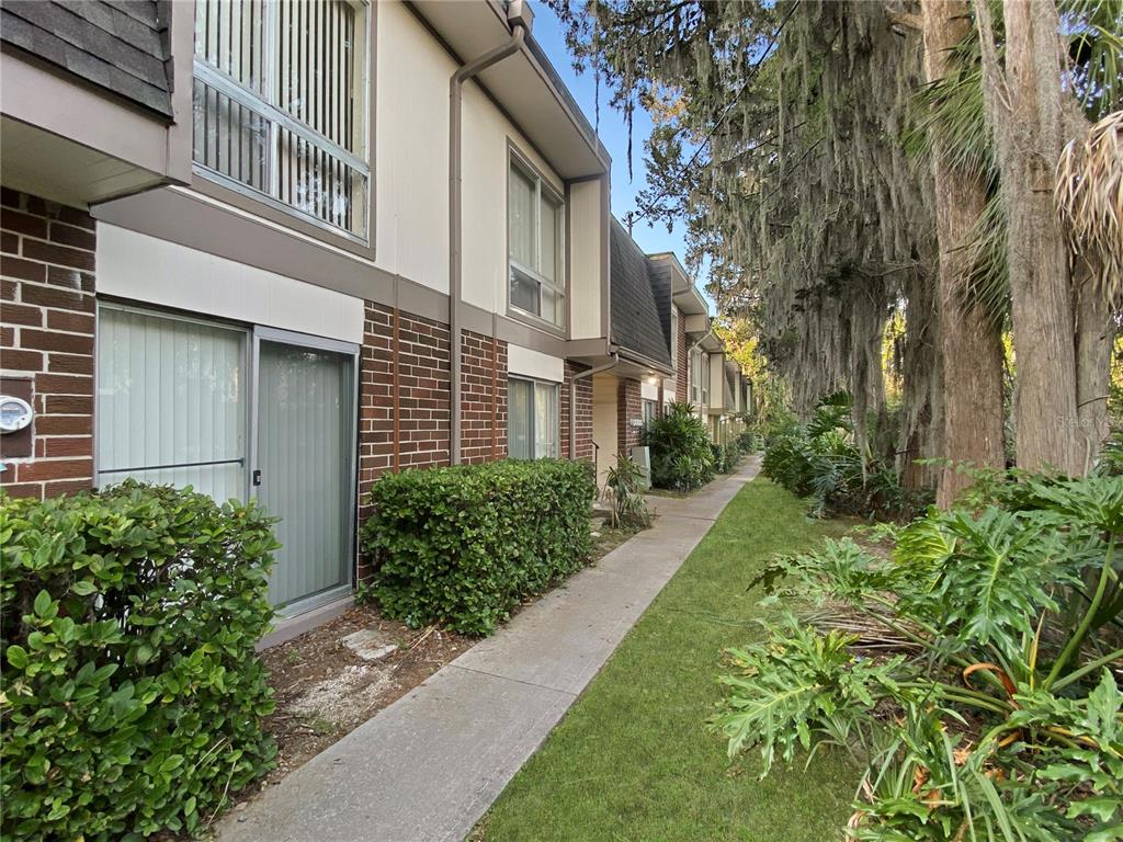 A concrete walkway leads past a row of townhomes with brick siding and sliding doors — 1700 SW 16TH COURT UNIT P6, GAINESVILLE, FL