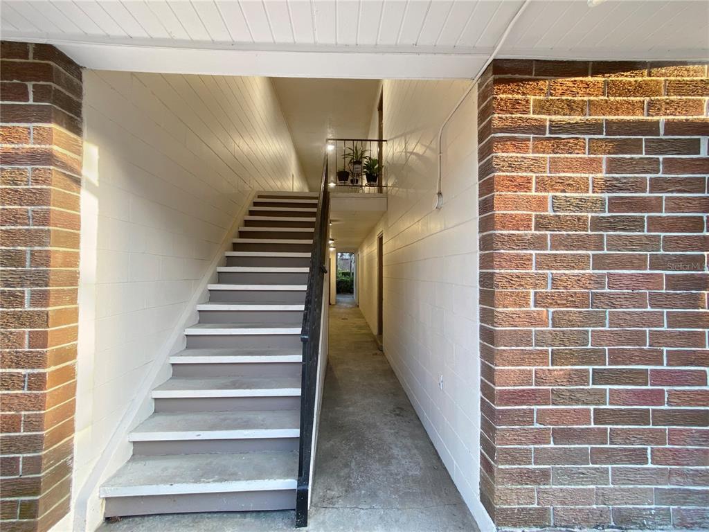 An exterior staircase leads to an upper-level walkway between two brick and white-walled buildings — 1700 SW 16TH COURT UNIT P6, GAINESVILLE, FL
