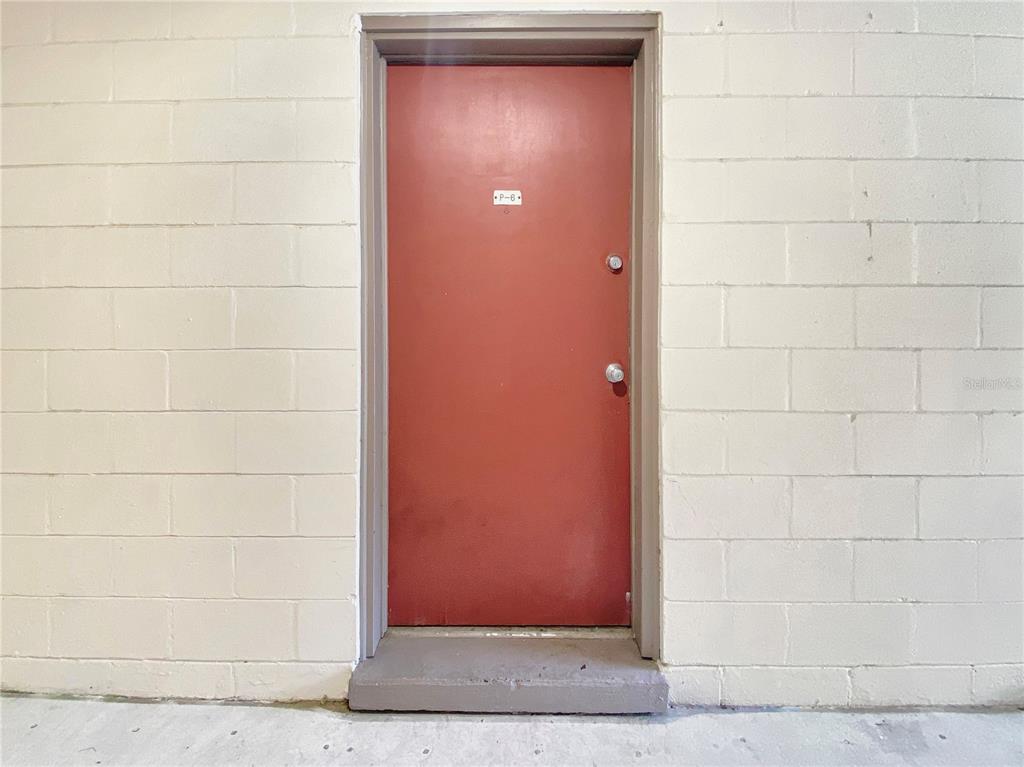 A red metal door with a small label is set into a beige block wall — 1700 SW 16TH COURT UNIT P6, GAINESVILLE, FL