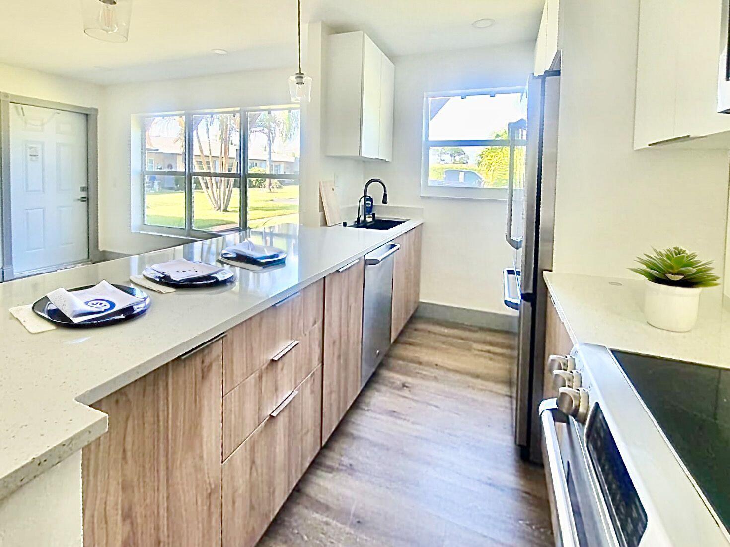 A modern kitchen features light wood cabinets, white countertops, stainless steel appliances, and wood flooring — 892 High Point Boulevard N # C, Delray Beach FL 33445, DELRAY BEACH, FL