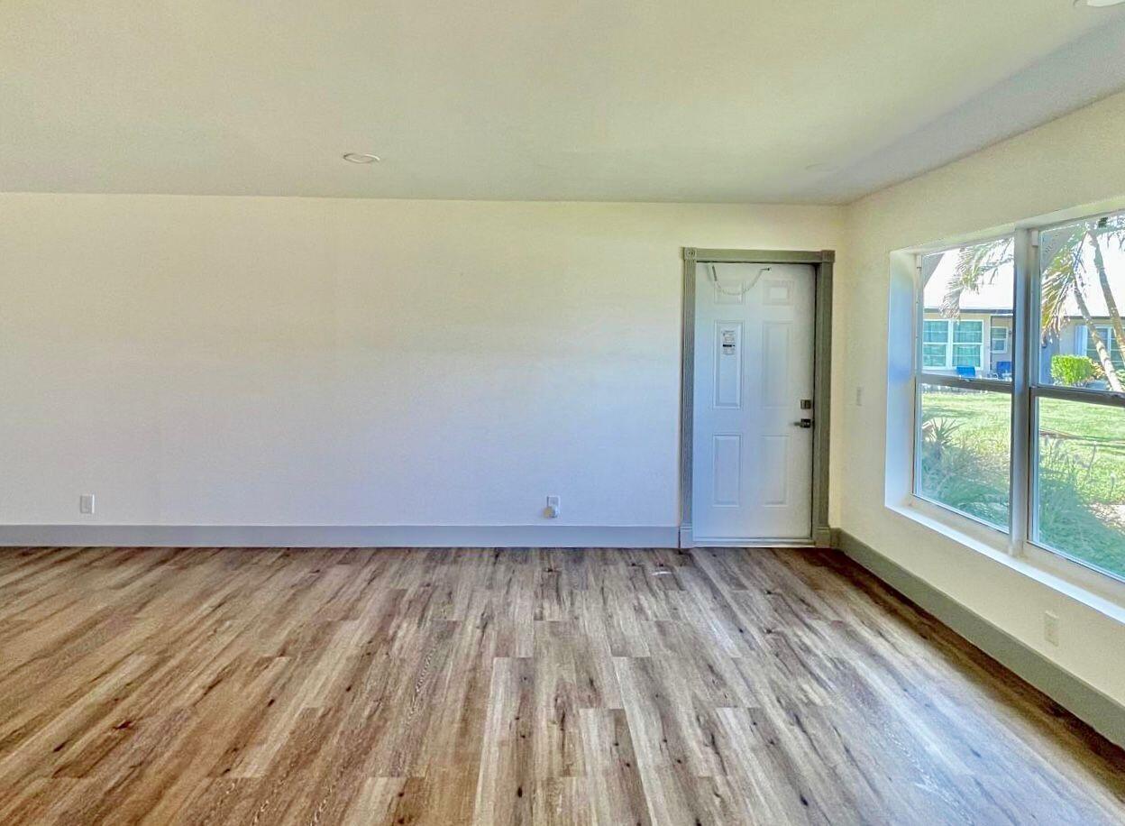 An empty room with light wood-look flooring, white walls, and a white exterior door — 892 High Point Boulevard N # C, Delray Beach FL 33445, DELRAY BEACH, FL