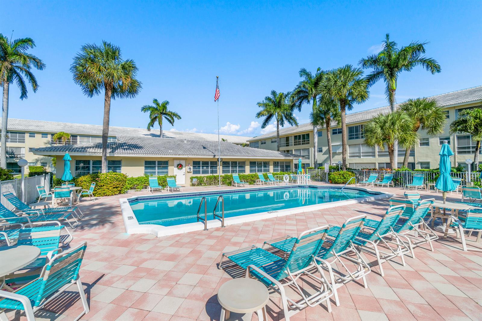 A swimming pool surrounded by lounge chairs and palm trees in front of apartment buildings — 1951 NE 39th Street # 131, Lighthouse Point FL 33064, LIGHTHOUSE POINT, FL