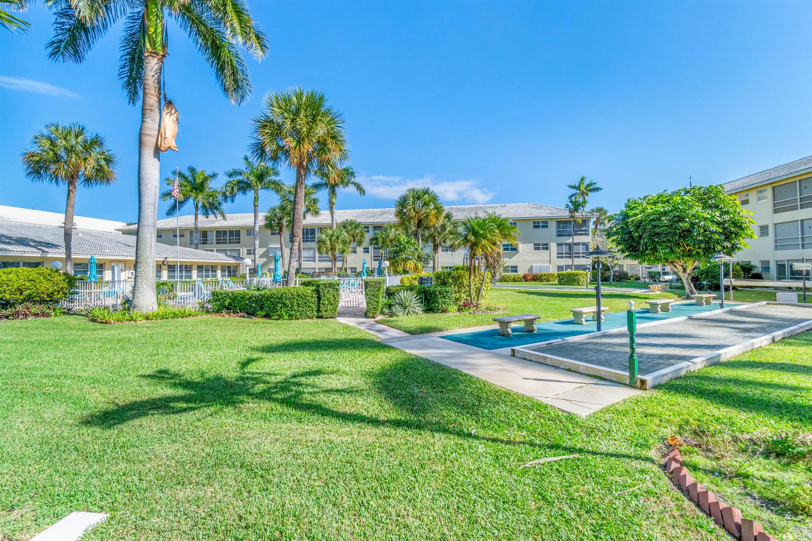 A grassy courtyard features palm trees, a shuffleboard court, and multi-story residential buildings — 1951 NE 39th Street # 131, Lighthouse Point FL 33064, LIGHTHOUSE POINT, FL
