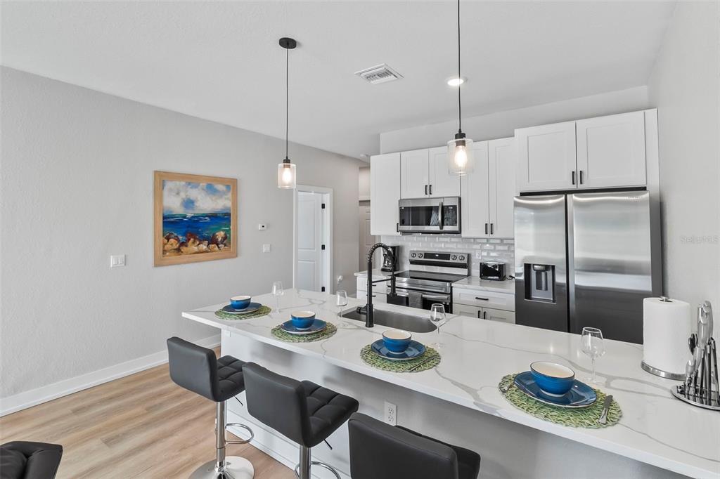 A modern kitchen features a white quartz island with bar seating and stainless steel appliances — 9155 AGATE STREET, PORT CHARLOTTE, FL