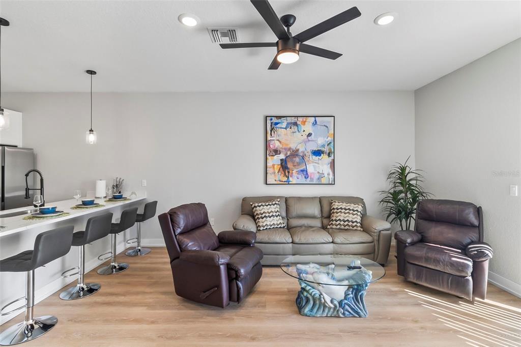A living room features a gray sofa, two brown recliners, and a kitchen breakfast bar — 9155 AGATE STREET, PORT CHARLOTTE, FL