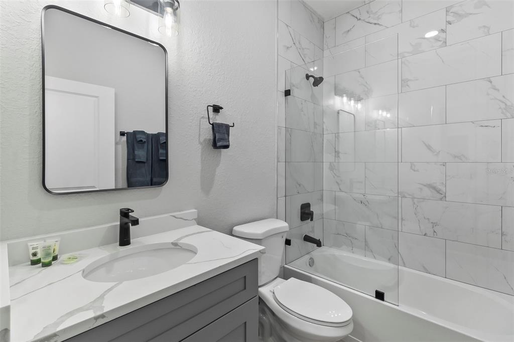 A bathroom features a gray vanity, marble-look countertop, toilet, and a tiled shower-tub combination — 9155 AGATE STREET, PORT CHARLOTTE, FL
