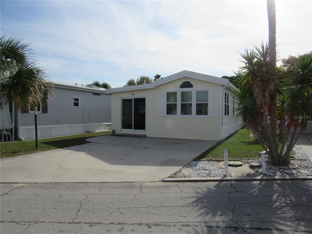 A light yellow manufactured home features a concrete driveway and a front sliding glass door — 9000 US HWY 192 UNIT 489, CLERMONT, FL