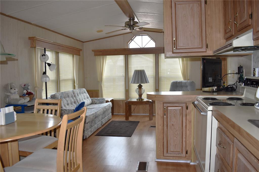 A living room and kitchen area with wood-look flooring, light wood cabinets, and a ceiling fan — 9000 US HWY 192 UNIT 489, CLERMONT, FL