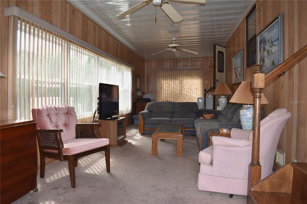 A living room features wood-paneled walls, carpeted flooring, two pink armchairs, and a grey sectional — 9000 US HWY 192 UNIT 489, CLERMONT, FL