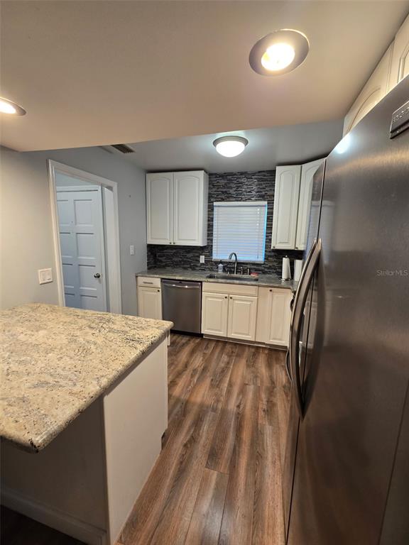 A kitchen features white cabinets, granite countertops, a stainless steel dishwasher, and wood-look flooring — 1118 VILLA LANE UNIT S, APOPKA, FL