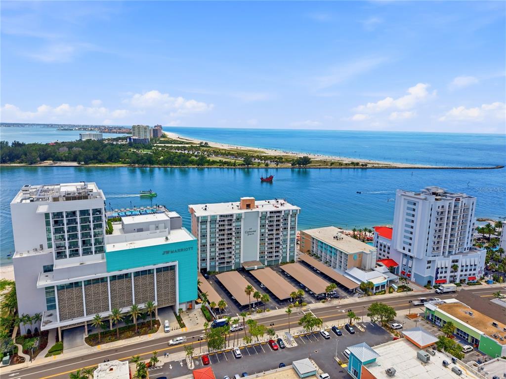 An aerial view shows several high-rise buildings along a waterfront with a beach in the distance — 675 S GULFVIEW BOULEVARD UNIT 206, CLEARWATER BEACH, FL