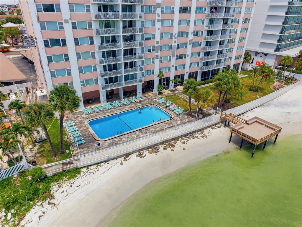An aerial view shows a multi-story pink apartment building with a pool and wooden pier — 675 S GULFVIEW BOULEVARD UNIT 206, CLEARWATER BEACH, FL