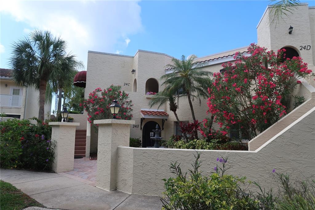 A two-story stucco building features a courtyard entrance with palm trees and flowering bushes — 6101 34TH STREET W UNIT 24C, BRADENTON, FL