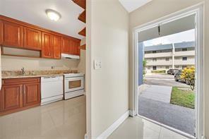 A kitchen with wood cabinets and white appliances next to an open door leading outside — 7897 Golf Circle Drive # 112, Margate FL 33063, MARGATE, FL