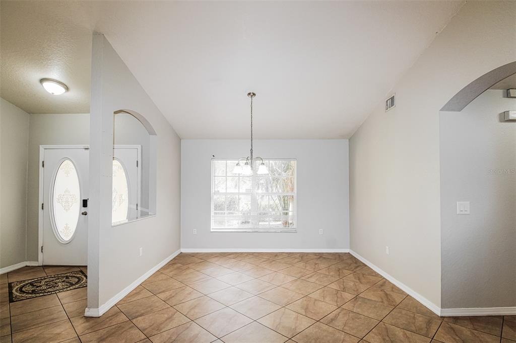An empty dining room with tile flooring, a central light fixture, and a large window — 6410 JAMAICA ROAD, SPRING HILL, FL