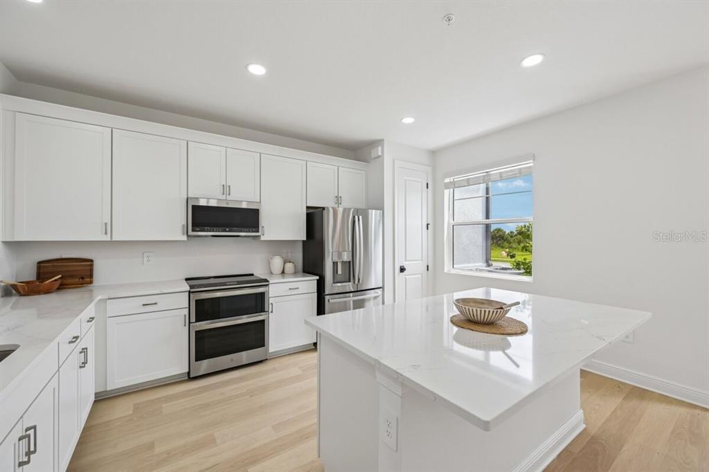 A modern kitchen features white cabinets, stainless steel appliances, and a large quartz-topped island — 17712 BROADLEAF LOOP, VENICE, FL