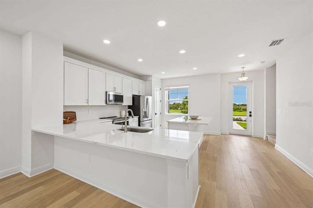 A modern kitchen features white cabinets, quartz countertops, a center island, and light wood flooring — 17712 BROADLEAF LOOP, VENICE, FL