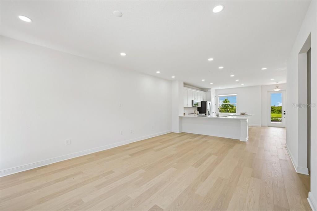 An open-concept living area with light wood flooring, recessed lighting, and a white kitchen — 17712 BROADLEAF LOOP, VENICE, FL
