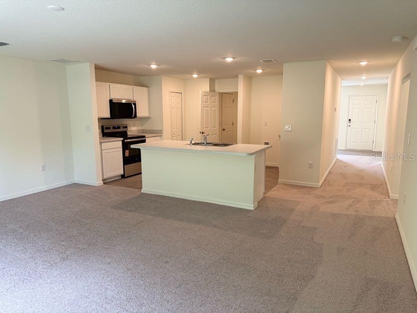 An open-concept kitchen with white cabinets and a central island overlooks a carpeted living area — 5718 N DECARLO DRIVE, CITRUS SPRINGS, FL