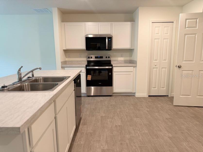 A kitchen features white cabinetry, stainless steel appliances, a double sink, and light wood-look flooring — 5718 N DECARLO DRIVE, CITRUS SPRINGS, FL
