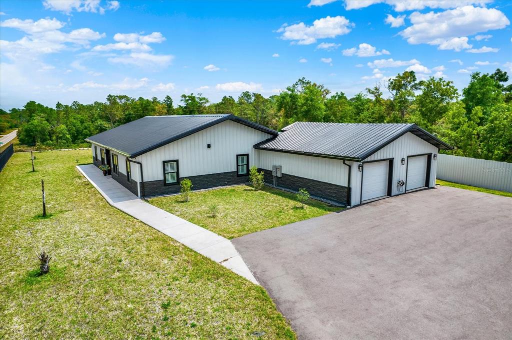 An exterior view of a modern white metal-sided house with a dark roof and garage — 34370 RICHARDSON BOULEVARD, WEBSTER, FL