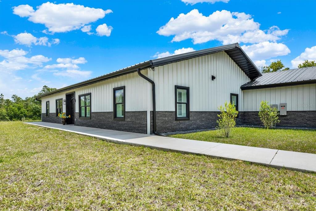 A single-story house with white metal siding, dark stone wainscoting, and a concrete walkway — 34370 RICHARDSON BOULEVARD, WEBSTER, FL