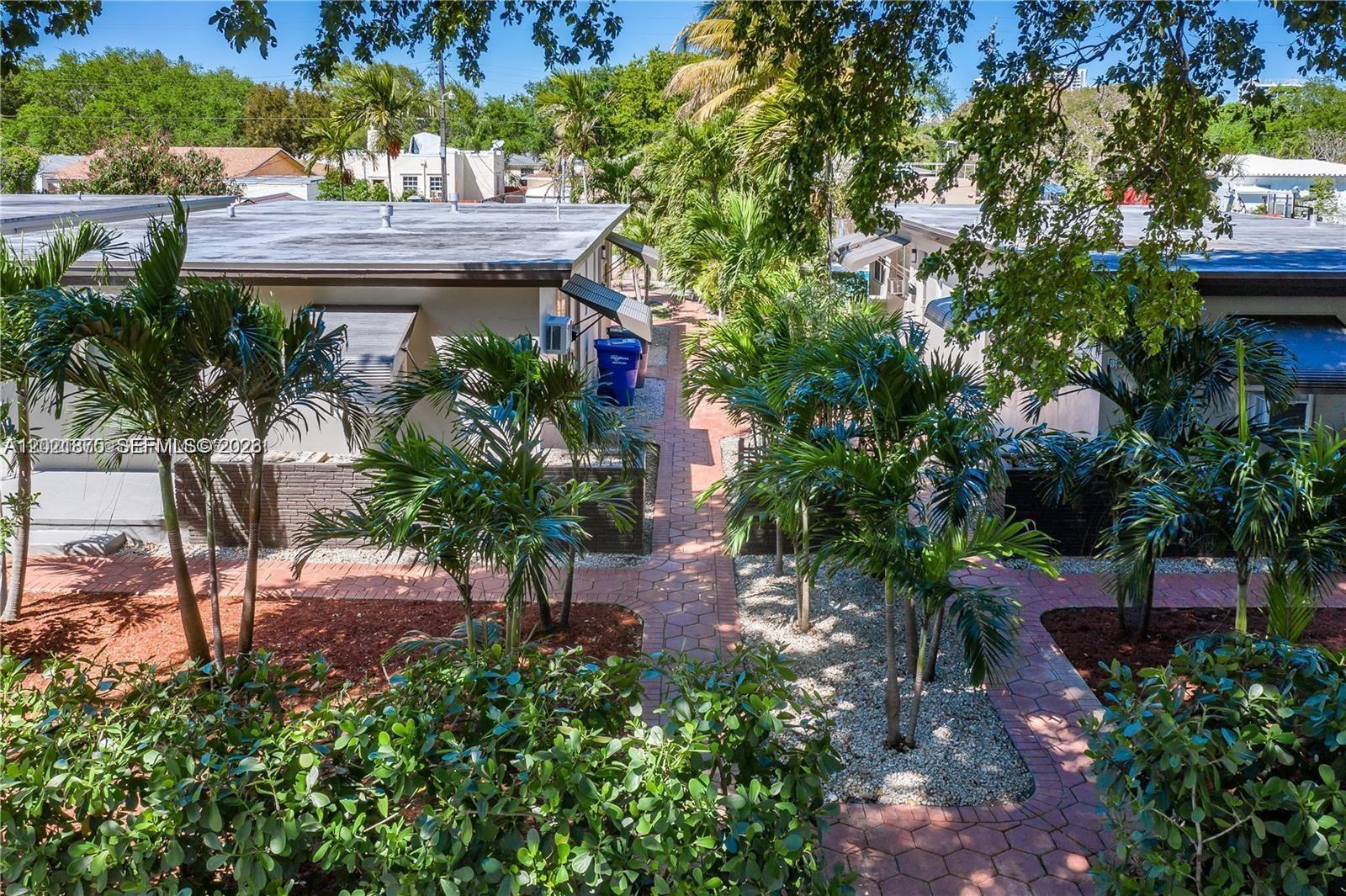 An exterior view shows a paved walkway between two single-story buildings surrounded by palm trees — 1925 Dewey St # 1925, Hollywood FL 33020, HOLLYWOOD, FL