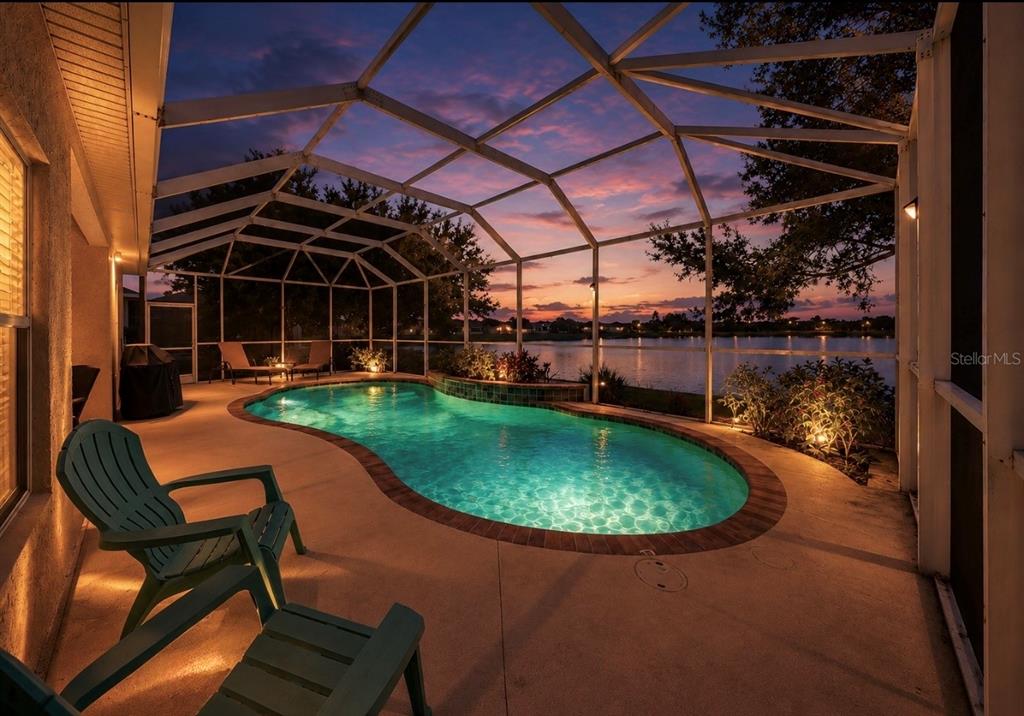 A screened-in patio features a kidney-shaped swimming pool overlooking a lake at sunset — 827 SEMINOLE SKY DRIVE, RUSKIN, FL