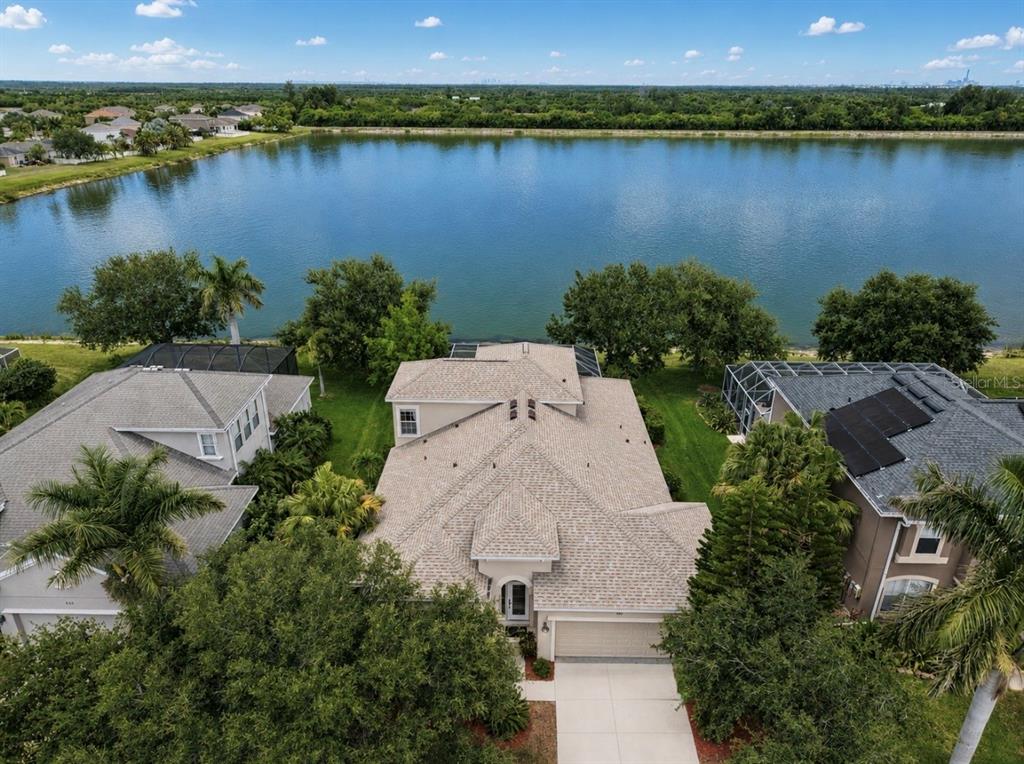 An aerial view shows a suburban house with a tan roof situated beside a lake — 827 SEMINOLE SKY DRIVE, RUSKIN, FL