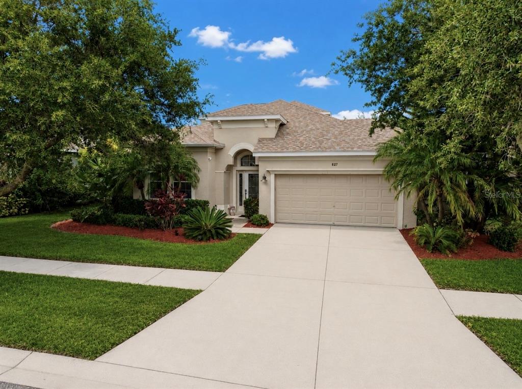 A single-story house with a beige stucco exterior, a two-car garage, and mature landscaping — 827 SEMINOLE SKY DRIVE, RUSKIN, FL