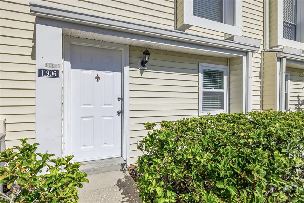 The exterior of a residential unit features a white front door and light-colored siding — 11906 CYPRESS HILL CIRCLE, TAMPA, FL