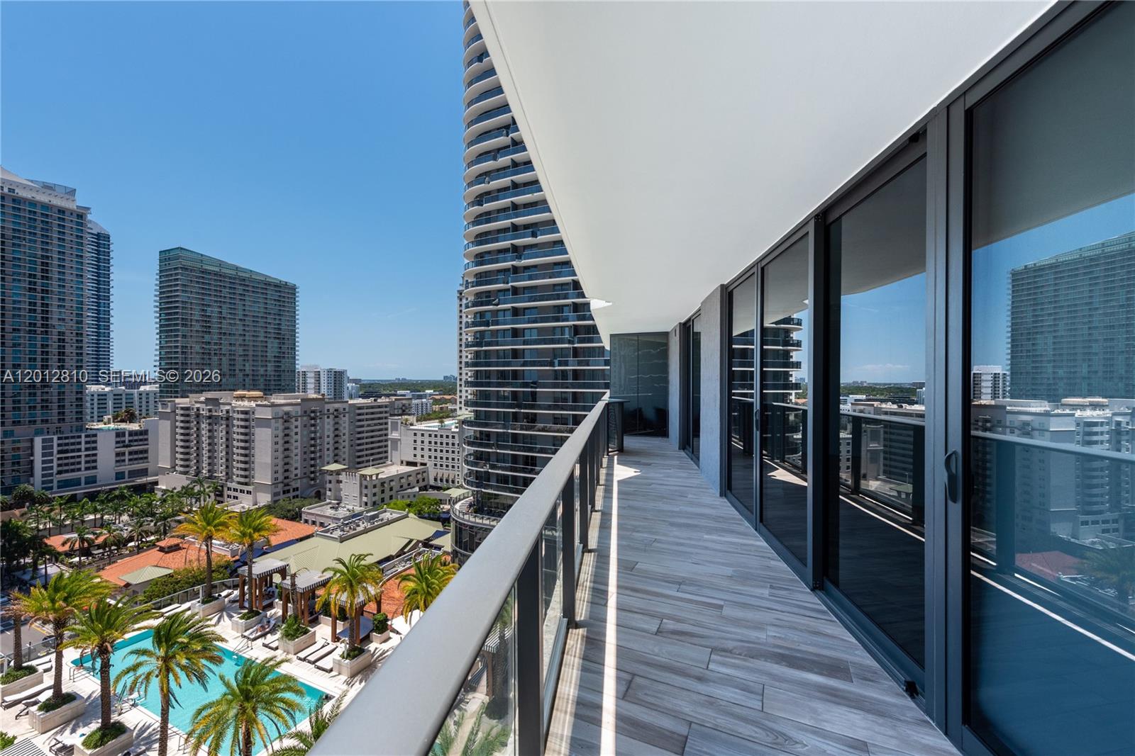 A high-rise balcony with wood-look tile flooring overlooks a swimming pool and city buildings — 801 S Miami Ave # 1602, Miami FL 33130, MIAMI, FL