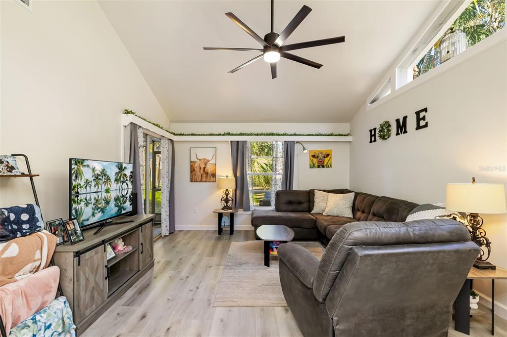 A living room features a vaulted ceiling, a sectional sofa, a television, and wood-look flooring — 5023 VILLAGE GARDENS DRIVE UNIT 29, SARASOTA, FL