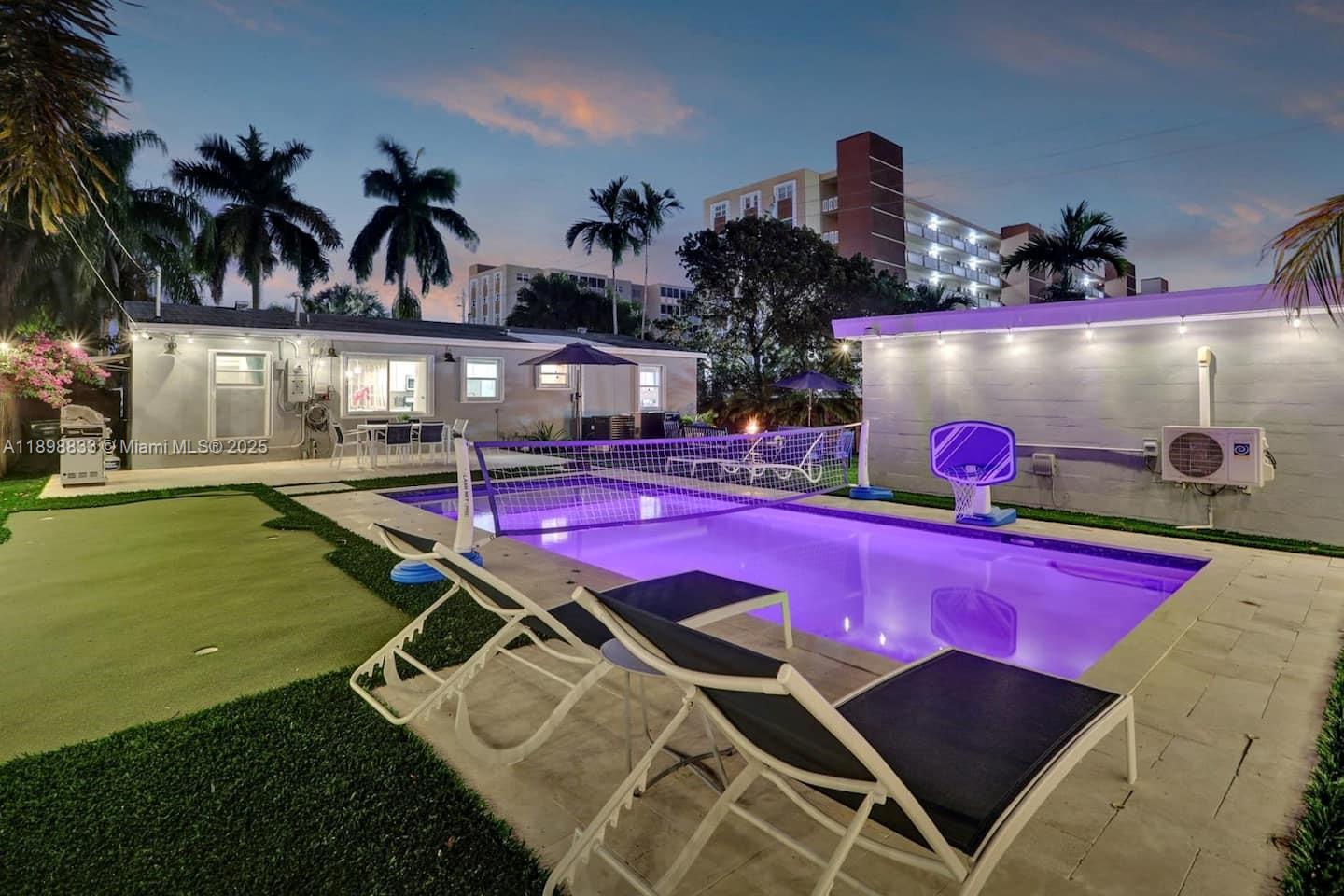 An outdoor swimming pool with a volleyball net and lounge chairs in a backyard setting — 1124 NE 6th St, Hallandale Beach FL 33009, HALLANDALE BEACH, FL