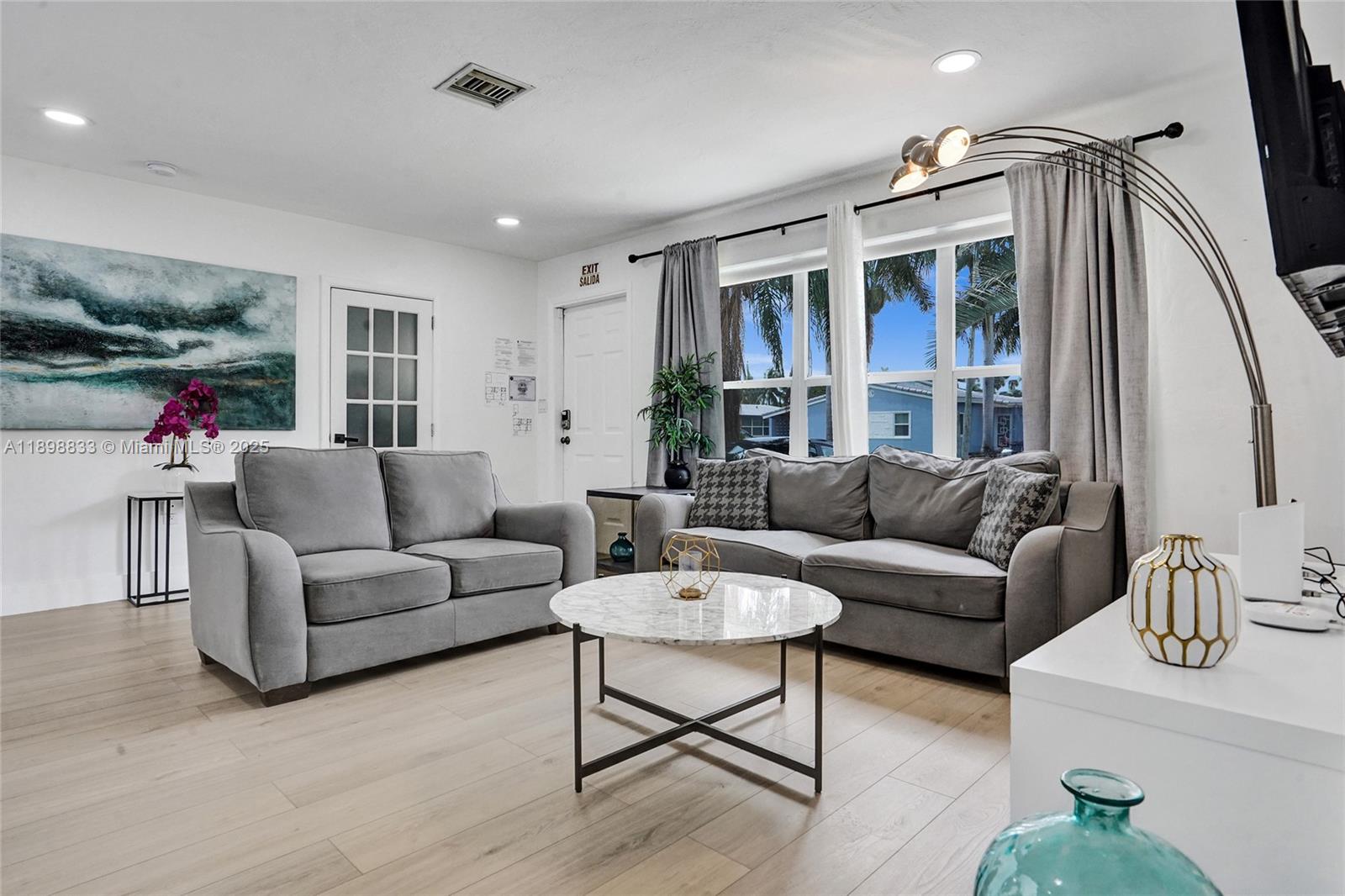 A living room features two gray sofas, a marble coffee table, and light wood flooring — 1124 NE 6th St, Hallandale Beach FL 33009, HALLANDALE BEACH, FL