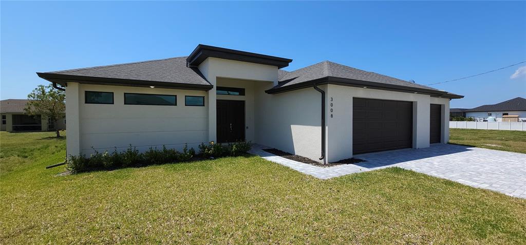 A modern single-story house features a light-colored stucco exterior, dark trim, and a paved driveway — 3008 NW 41ST AVENUE, CAPE CORAL, FL