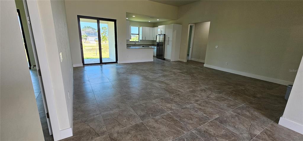 An open-concept living area features large tile flooring, a kitchen with white cabinets, and sliding doors — 3008 NW 41ST AVENUE, CAPE CORAL, FL