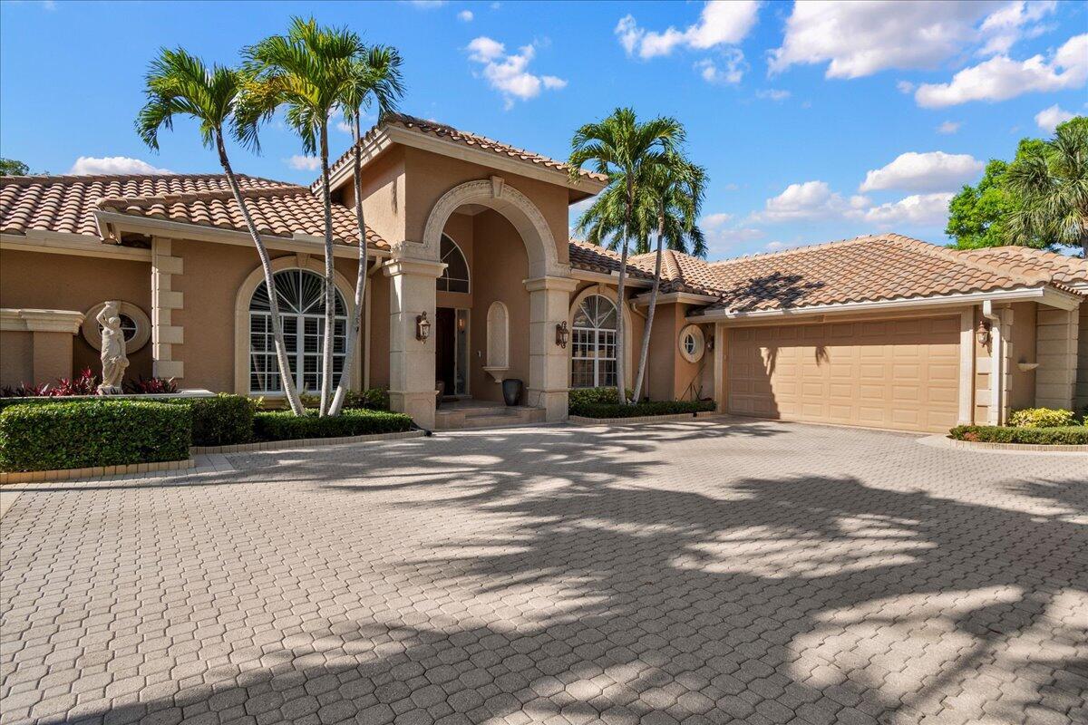 A tan stucco house with a tiled roof, arched entryway, and a paved circular driveway — 1338 Breakers West Boulevard, West Palm Beach FL 33411, WEST PALM BEACH, FL