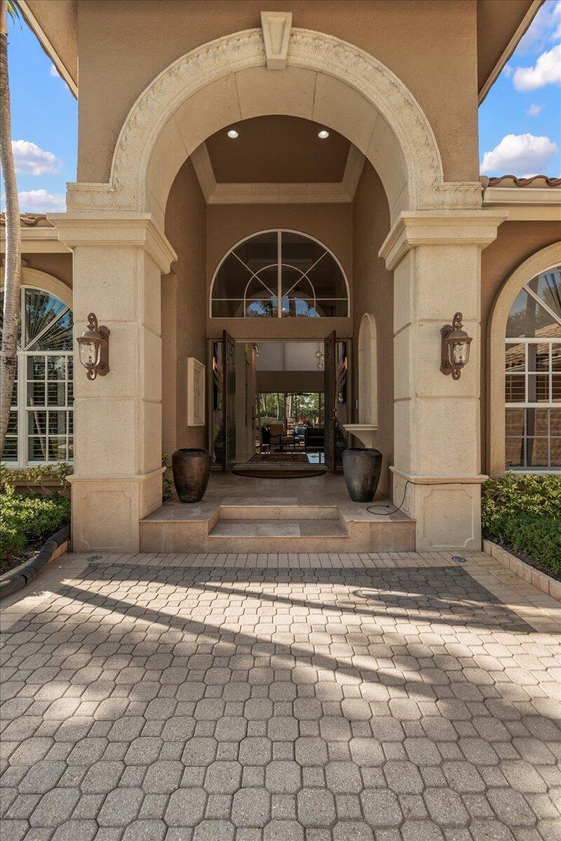 A stone-paved entryway leads to a grand arched doorway with two large decorative urns — 1338 Breakers West Boulevard, West Palm Beach FL 33411, WEST PALM BEACH, FL