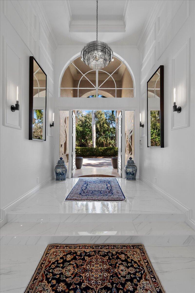A bright entryway features white marble floors, a crystal chandelier, and a view of greenery — 1338 Breakers West Boulevard, West Palm Beach FL 33411, WEST PALM BEACH, FL