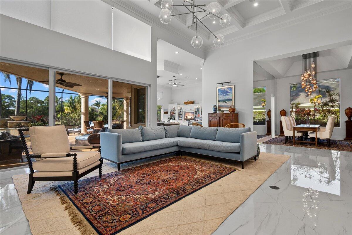 A spacious living room features a blue sectional, an ornate rug, and a large chandelier — 1338 Breakers West Boulevard, West Palm Beach FL 33411, WEST PALM BEACH, FL