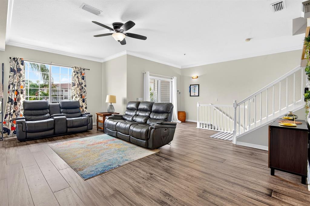 A living room features wood-look flooring, two leather reclining sofas, a colorful rug, and stairs — 1014 34TH DRIVE W, PALMETTO, FL