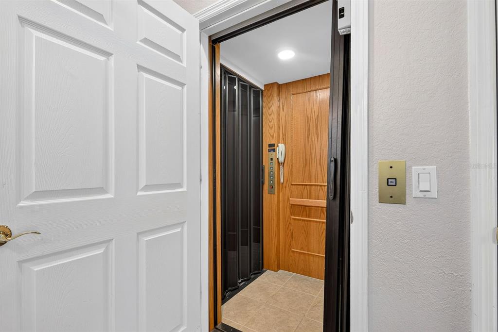 An open door reveals a home elevator with wood paneling, a folding gate, and tile flooring — 1014 34TH DRIVE W, PALMETTO, FL