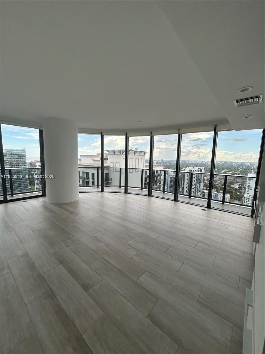 An empty room with light wood-look flooring and floor-to-ceiling windows overlooking a city skyline — 55 SW 9th St # 3506, Miami FL 33130, MIAMI, FL