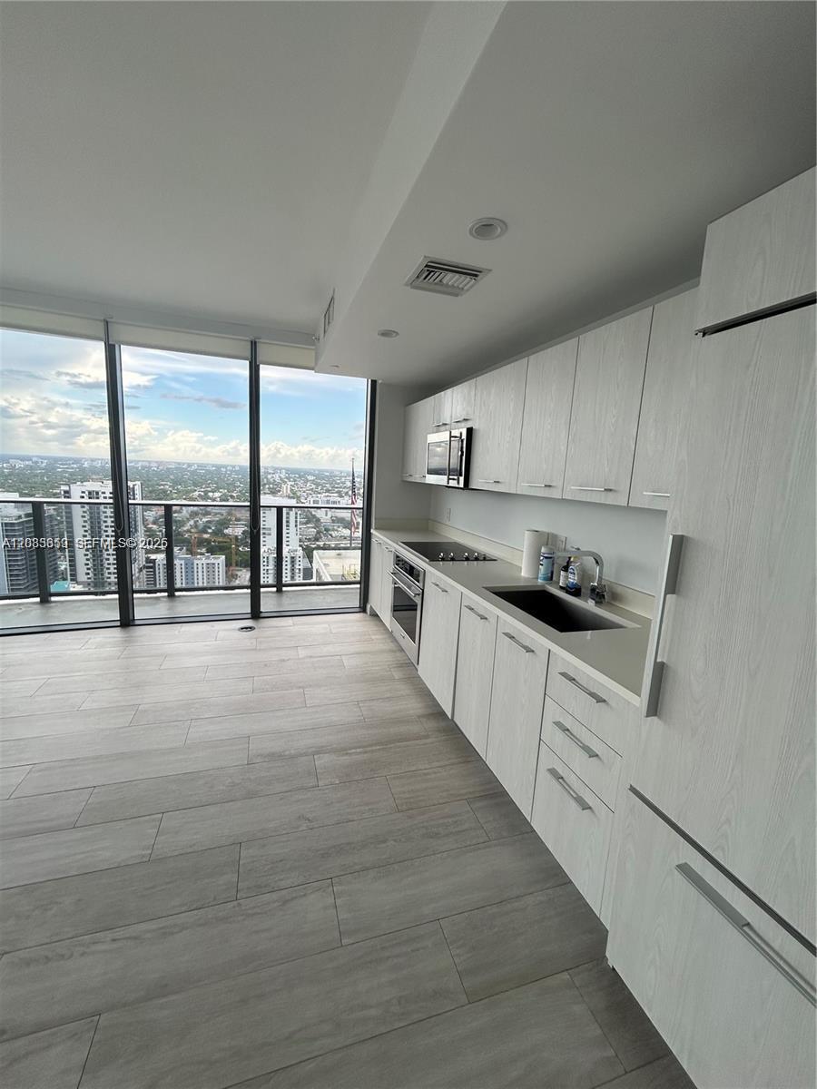 A modern kitchen features light wood-grain cabinets, stainless steel appliances, and floor-to-ceiling windows with views — 55 SW 9th St # 3506, Miami FL 33130, MIAMI, FL